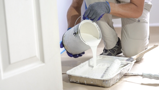 professional painter pouring a gallon of paint into a paint tray