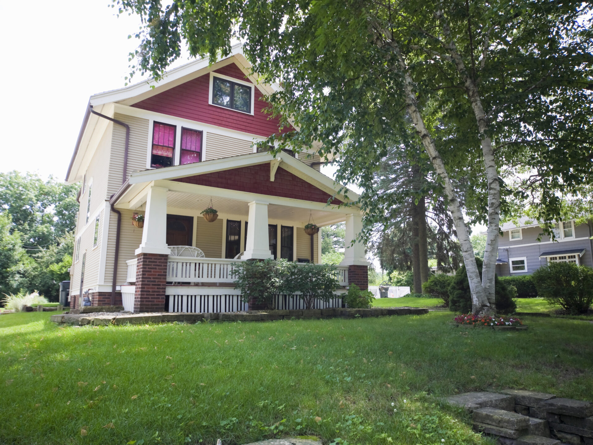 Two-story house with red siding, white trim, and a covered front porch surrounded by green lawn and trees.